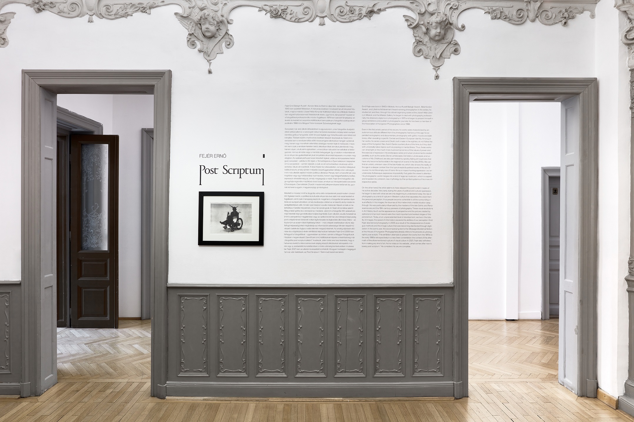 The Post Scriptum exhibition title, wall text and a framed photograph between two doorways in an ornate gallery.
