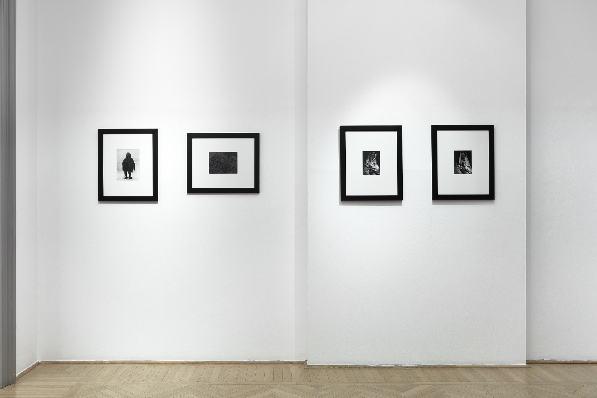 Four framed photographs in two pairs on a white exhibition wall above a parquet floor.