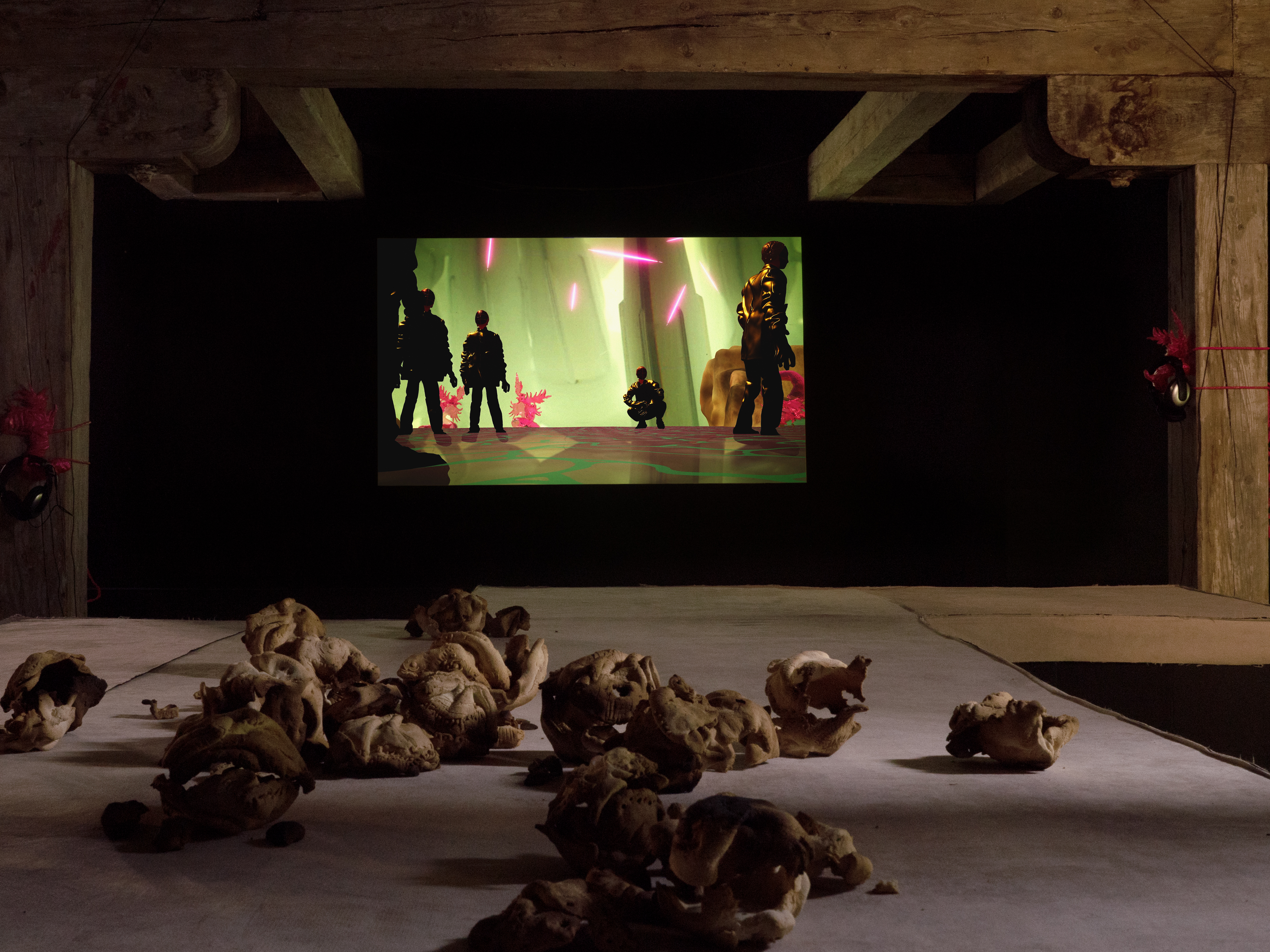 A glowing green video projection beneath timber beams, with sculptural forms scattered across the floor of the Surface Tension exhibition.
