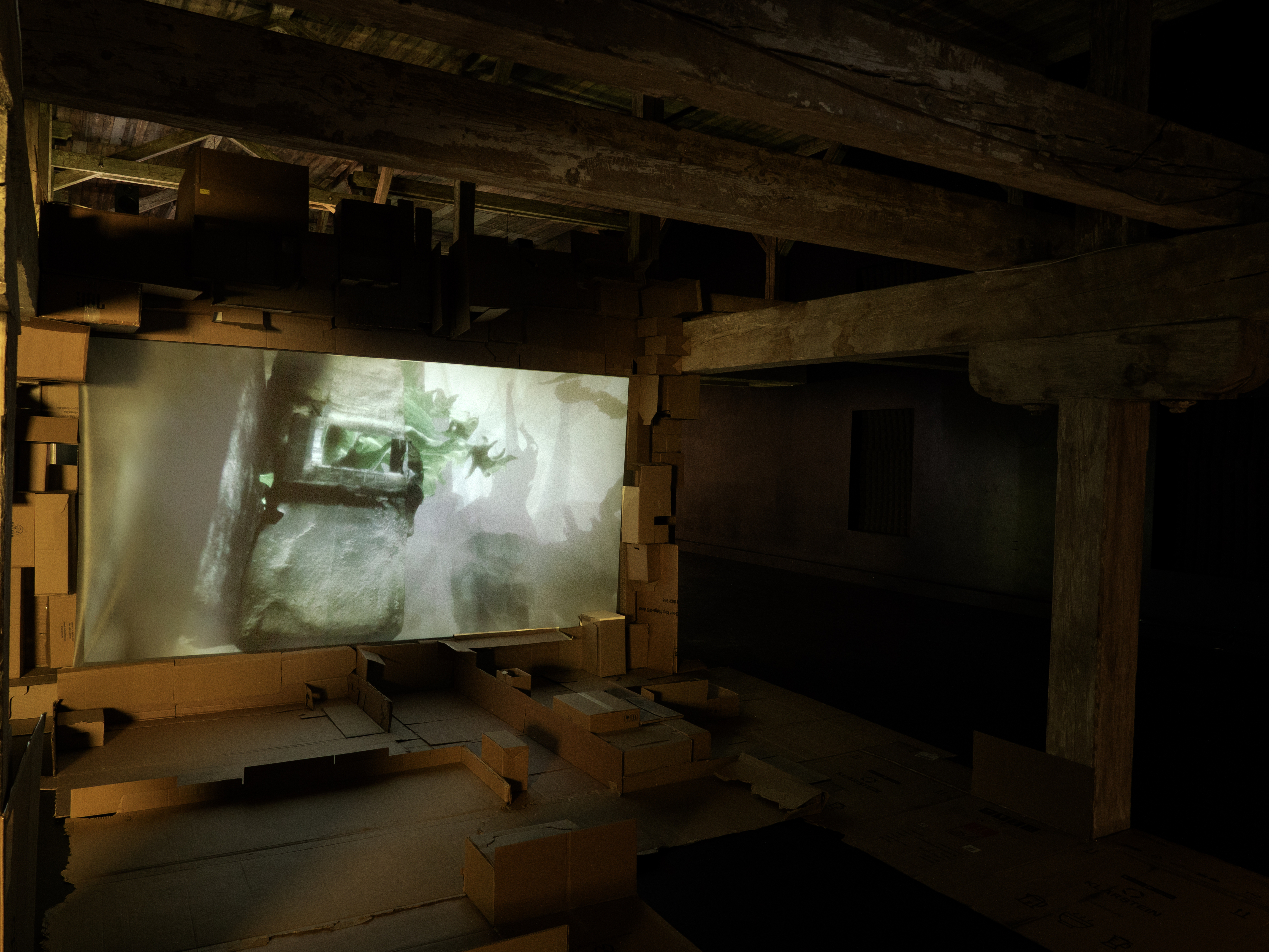 A video projection framed by stacked cardboard boxes inside the timber structure of the attic gallery.